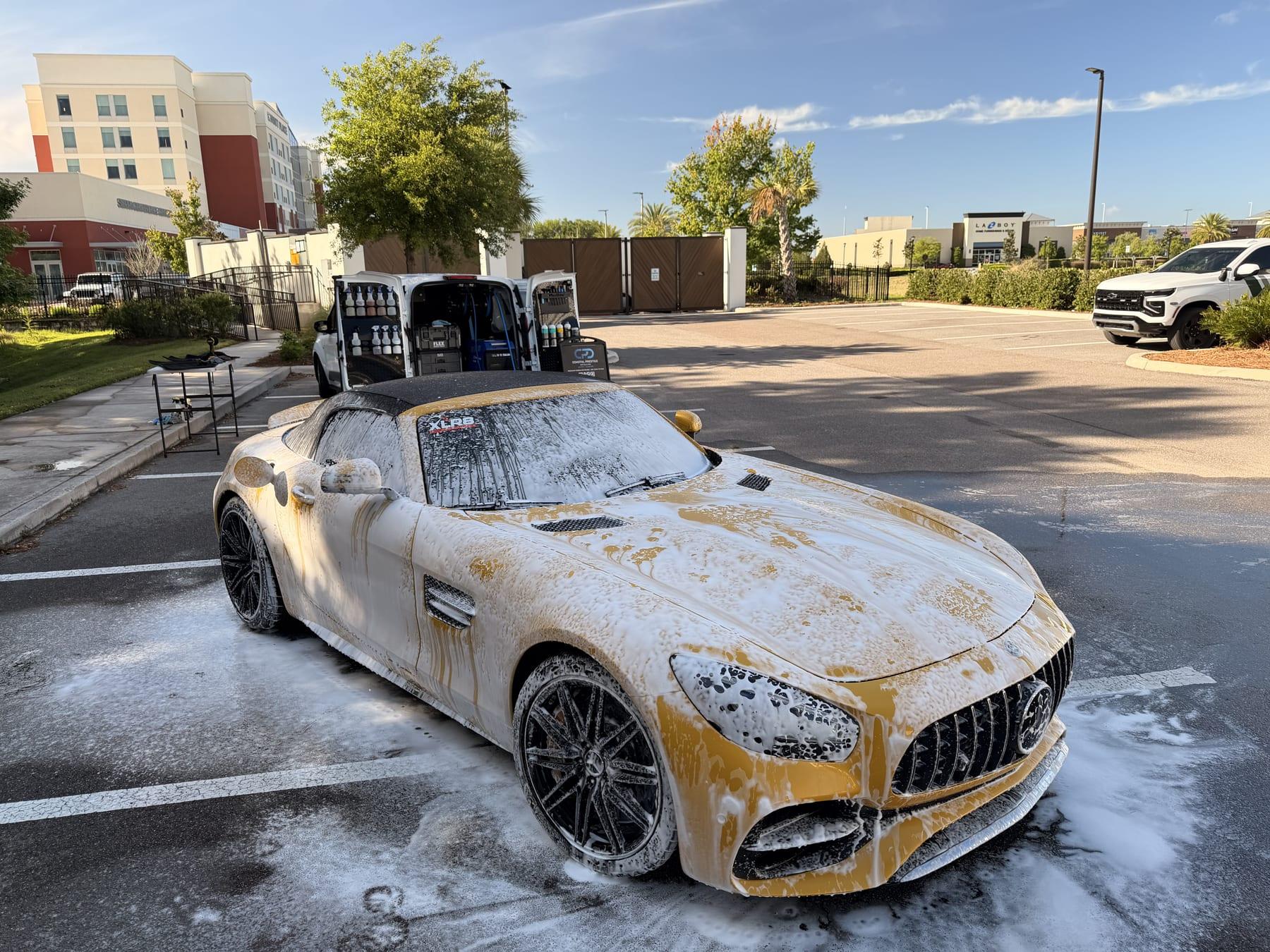 Yellow Mercedes-AMG GT C Roadster covered in foam during a mobile detail in Wesley Chapel, with the Coastal Prestige Detailing van alongside