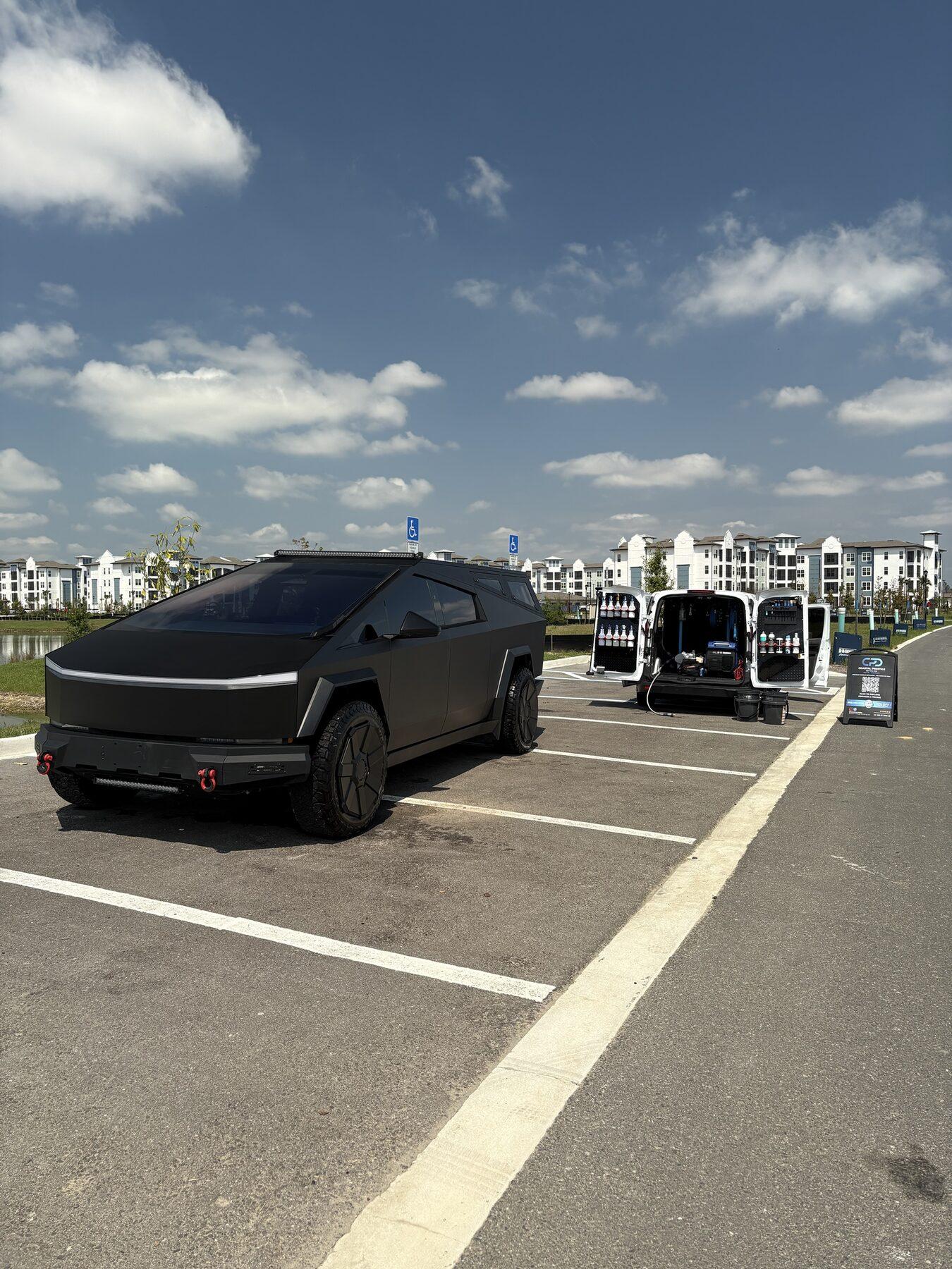 Matte black Tesla Cybertruck finished after a detail, with the Coastal Prestige Detailing van open alongside in a Tampa Bay car park