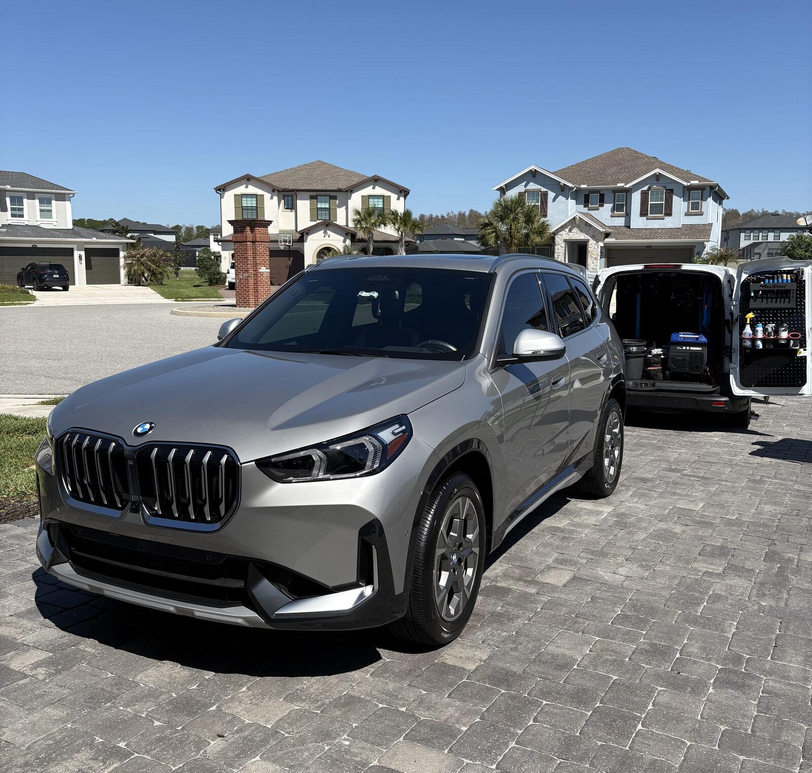 Finished silver BMW X1 on a paver driveway with the Coastal Prestige Detailing van open behind it